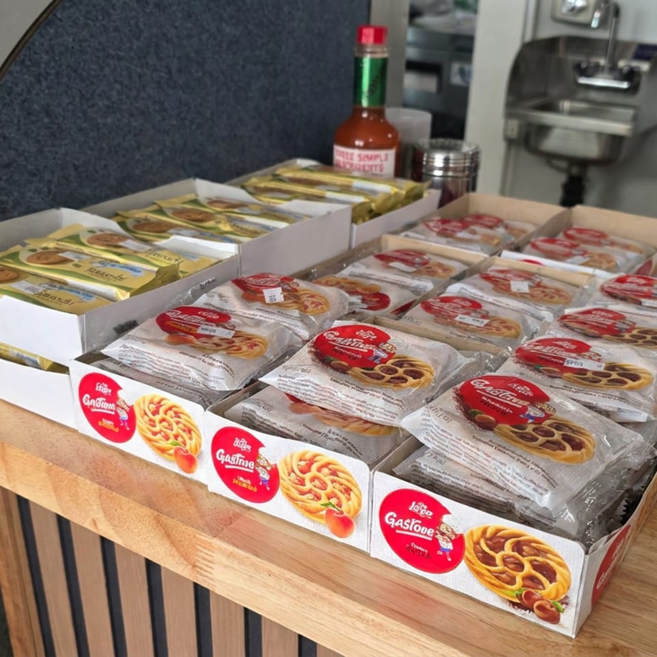 Packaged pastries and pretzels arranged in display boxes on a wooden counter beside a hot sauce bottle.