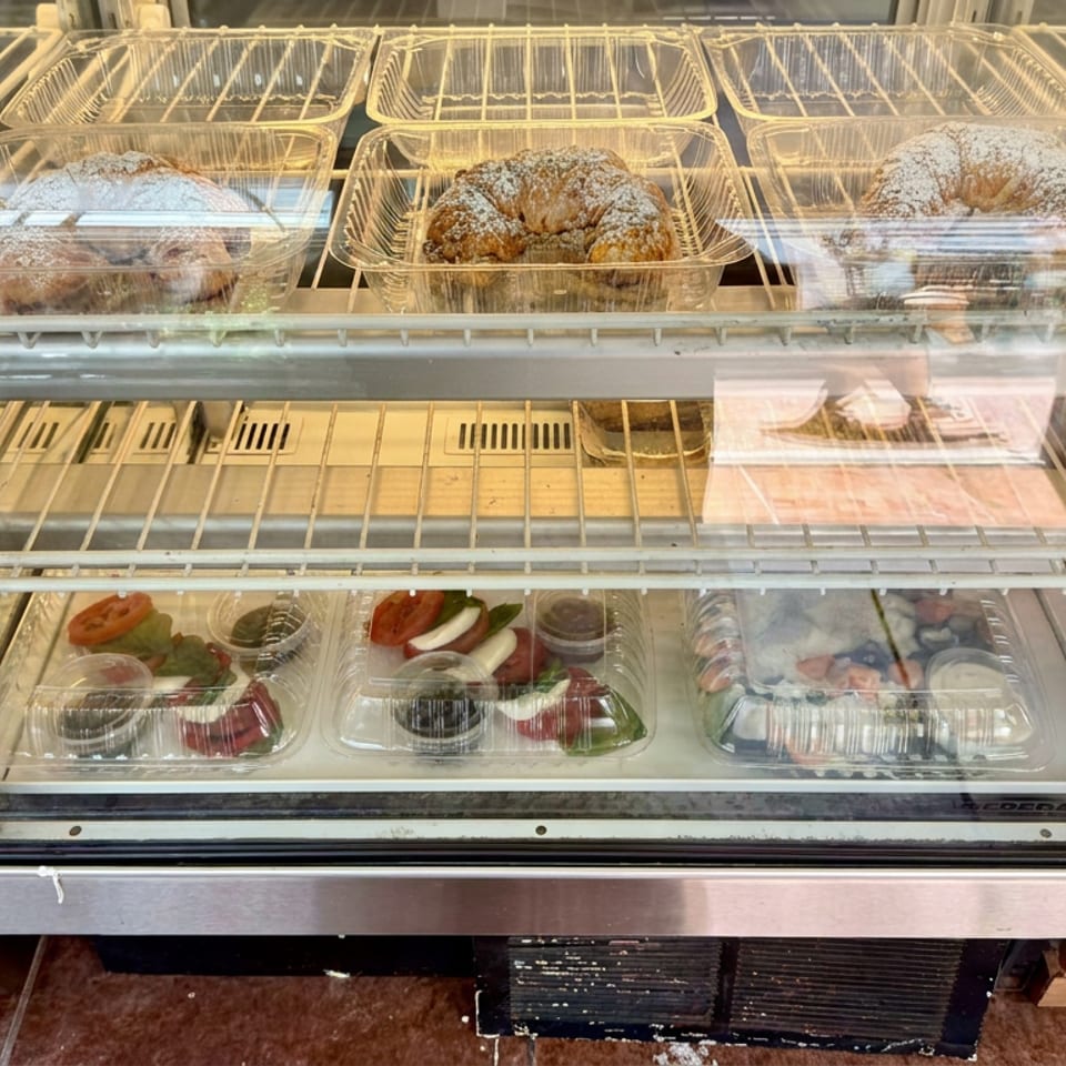 Refrigerated bakery display case holding powdered sugar pastries and assorted packaged desserts.