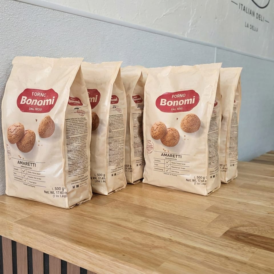 Bags of Forno Bonomi amaretti cookies displayed on a wooden counter beside a commercial oven.